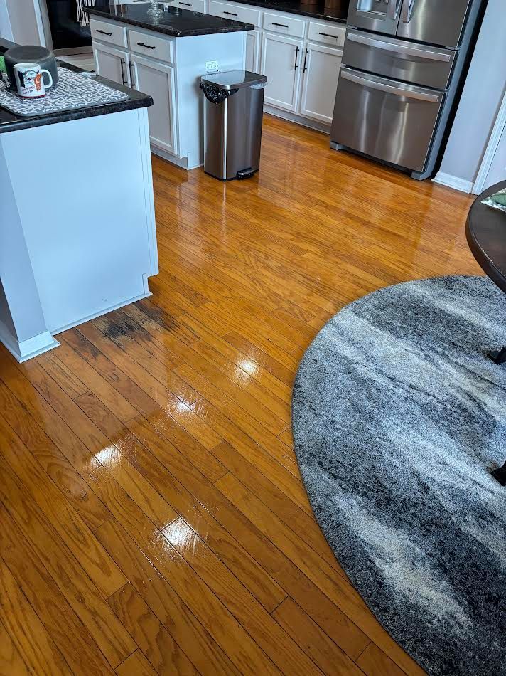 Wooden kitchen floor with shiny finish; white cabinets and island; stainless steel appliances.