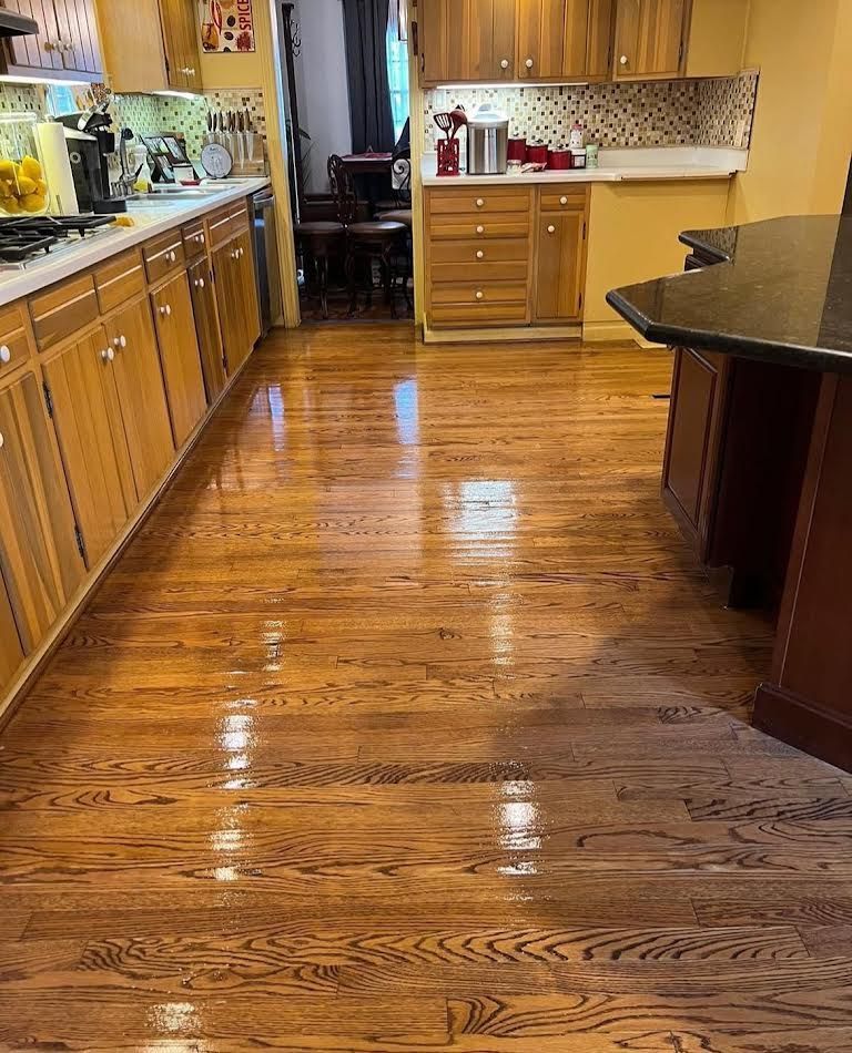 Shiny hardwood floor in a kitchen with wooden cabinets, a kitchen island, and a view into a dining room.