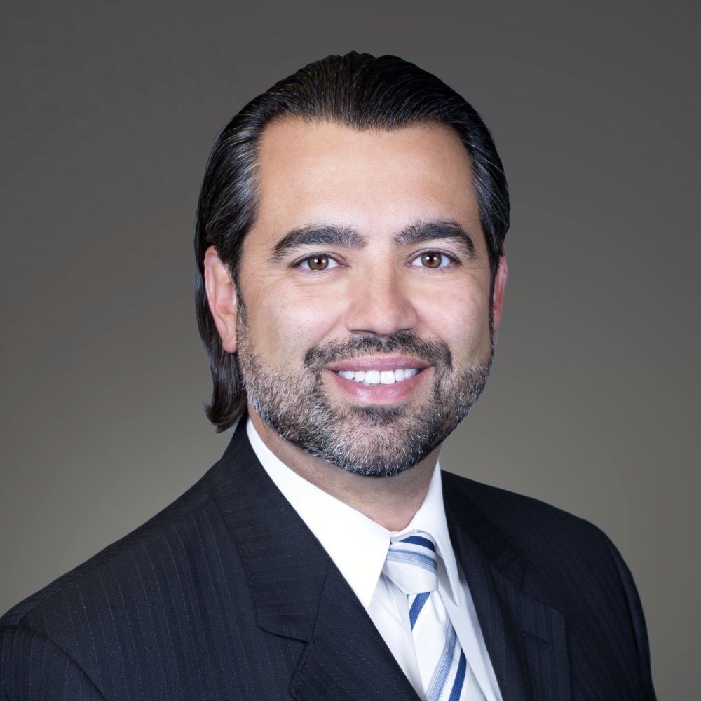 Man in suit smiles at the camera, against a neutral background.