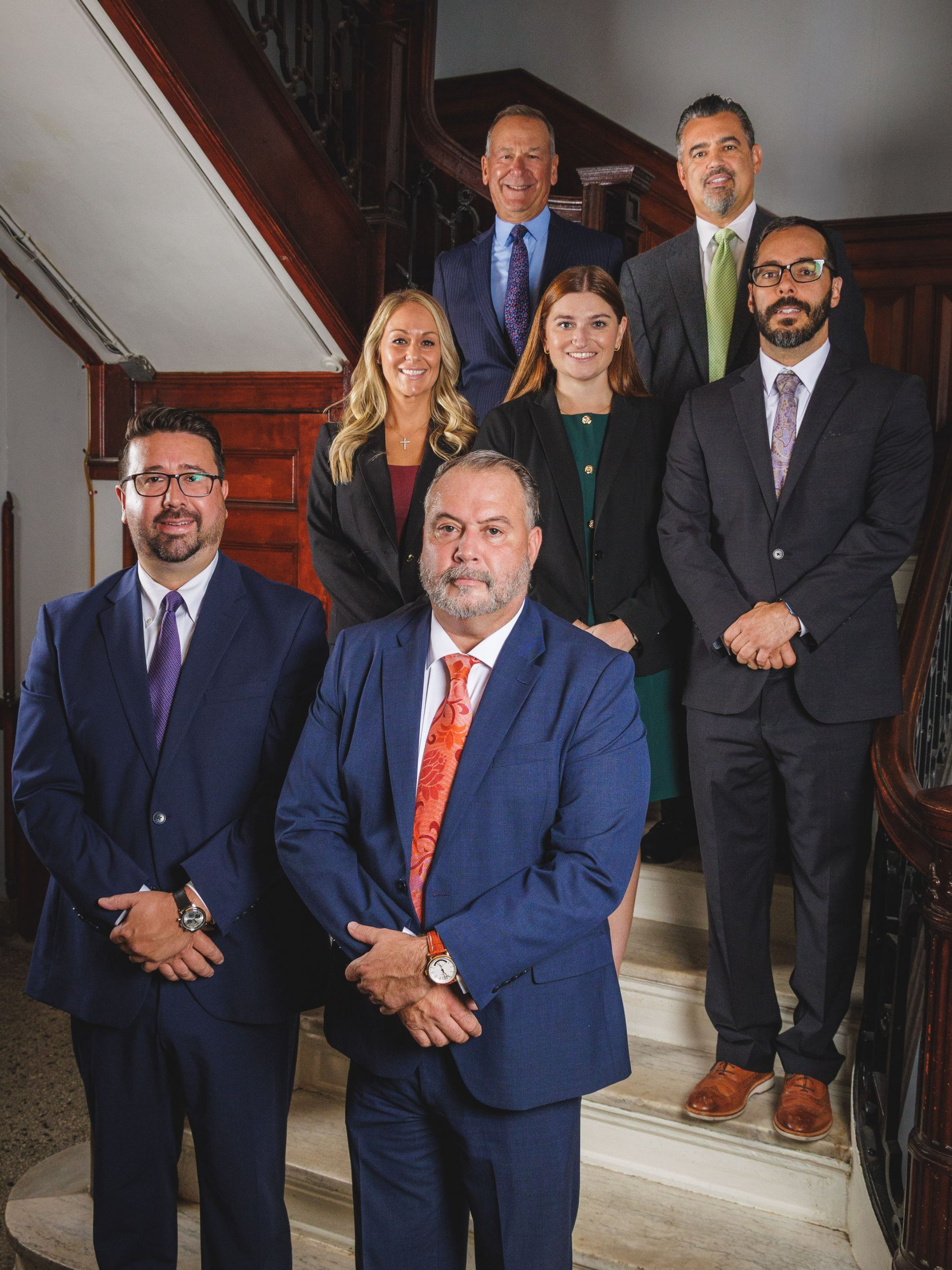 Group of people on a staircase. Most wear suits; some smiling, posing. Interior setting.