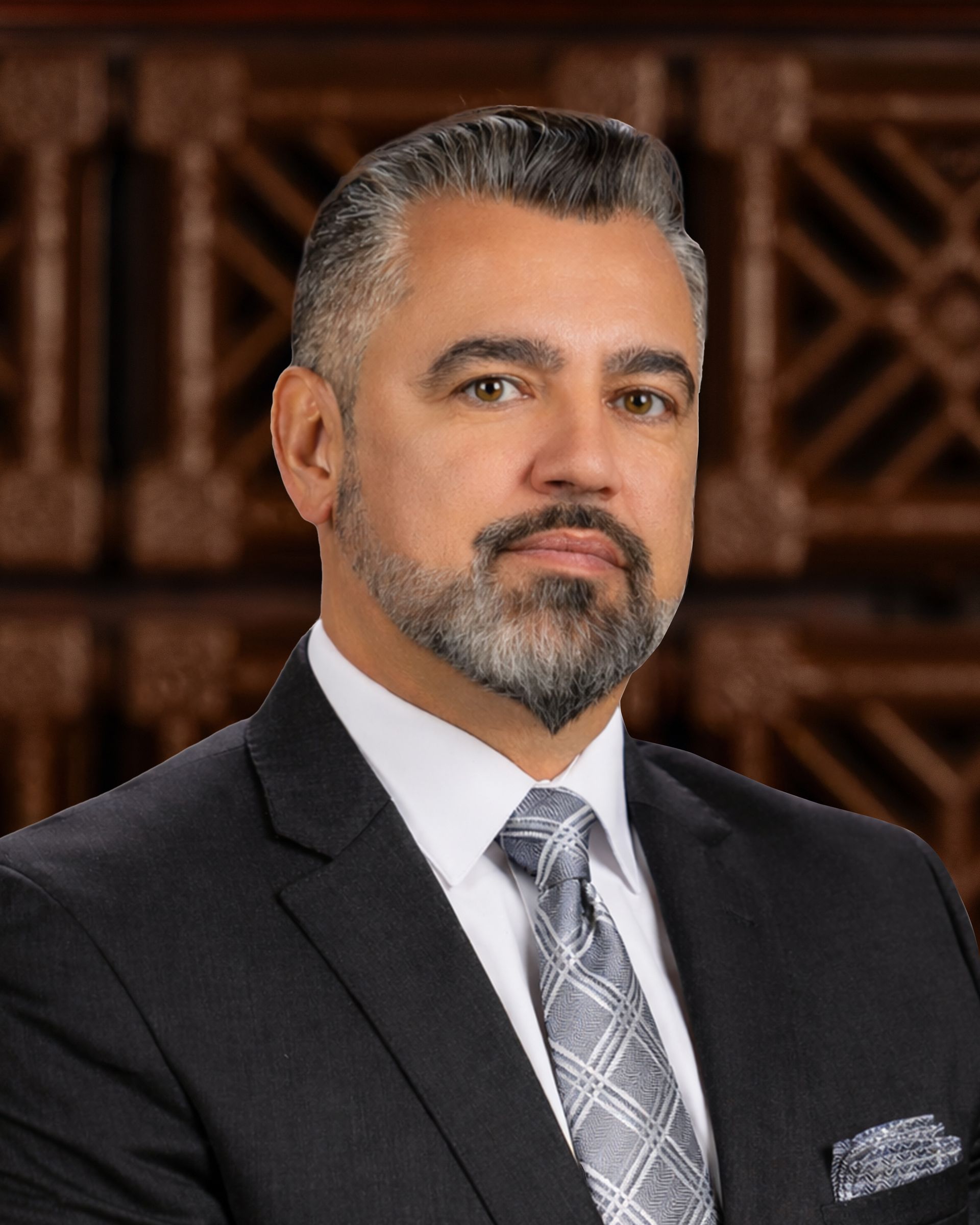 Man in suit and tie, looking at the viewer. Background is dark wood paneling.