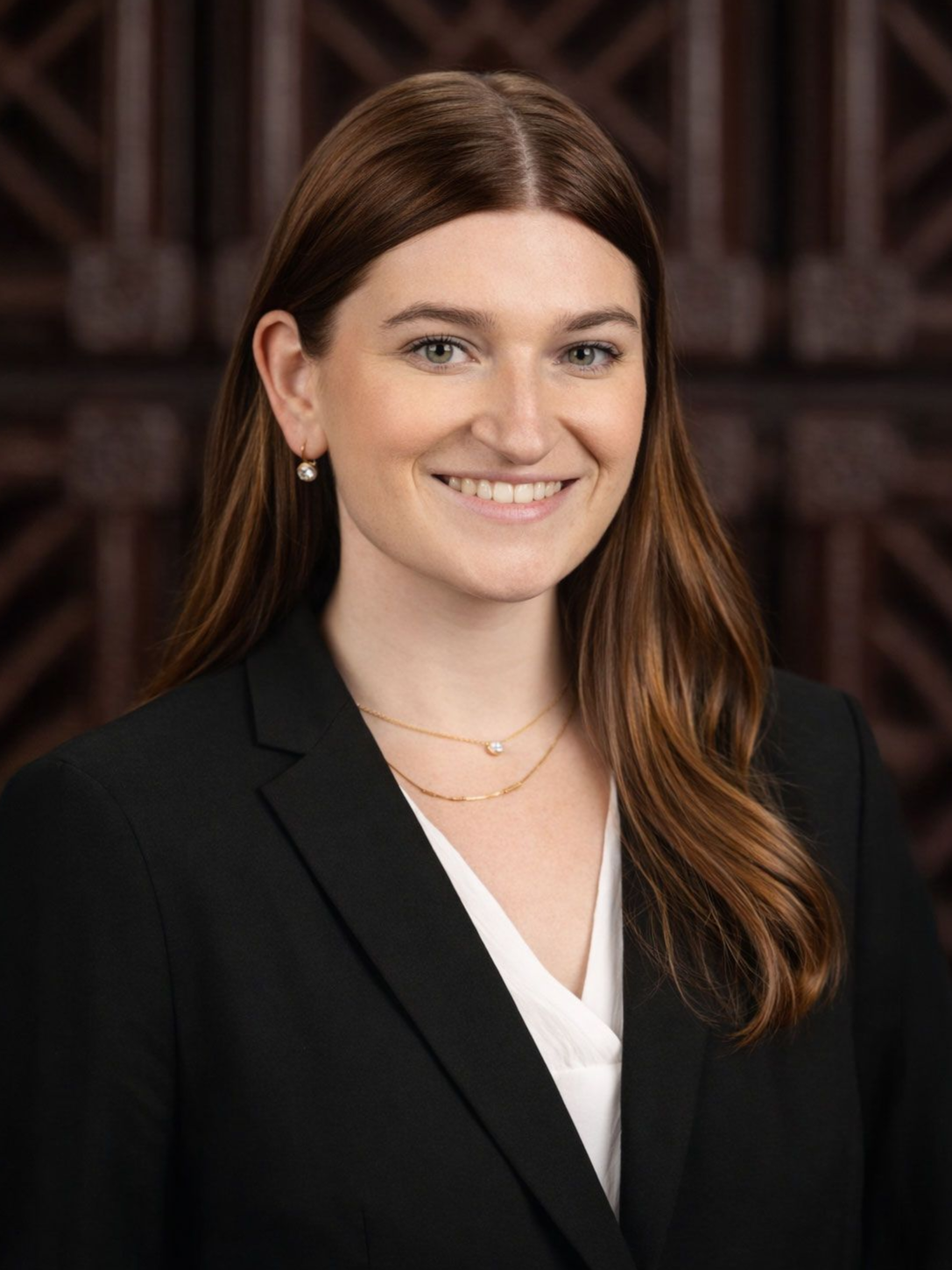 Woman in business attire smiles at the camera, dark blazer over a green top, brown hair.