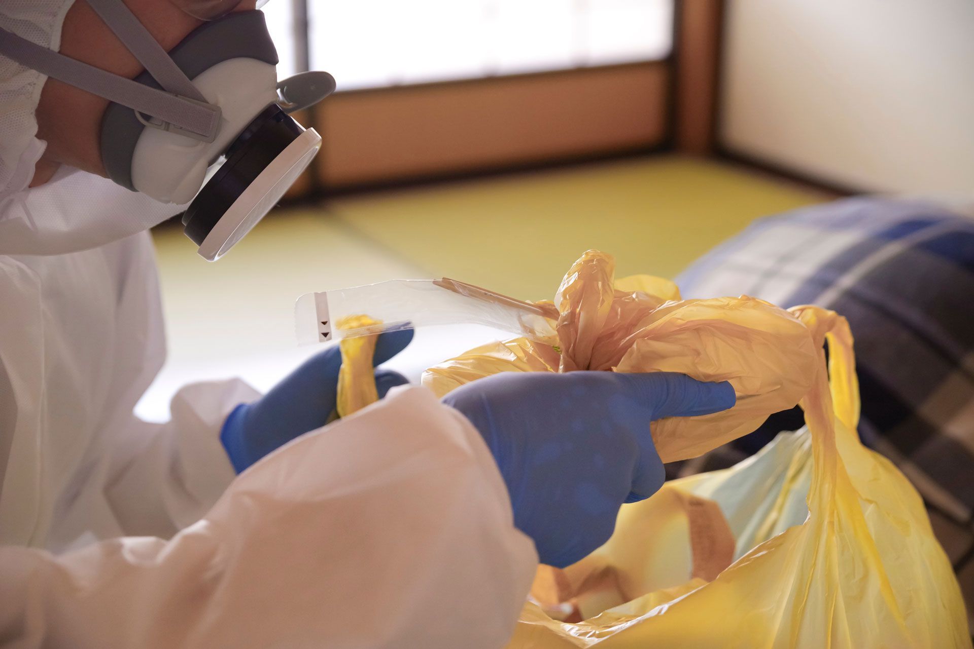 Person in protective gloves sorting trash into a yellow plastic bag indoors