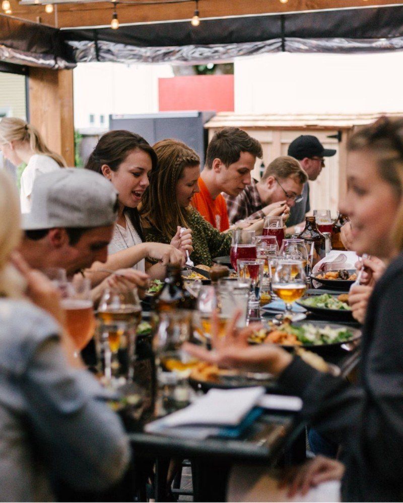 Un gruppo di persone è seduto a dei tavoli e mangia cibo e beve birra.