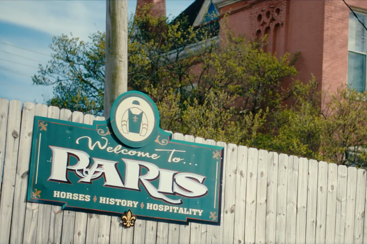 Sign welcoming to Paris, with a horse silhouette. Fence and building in background.
