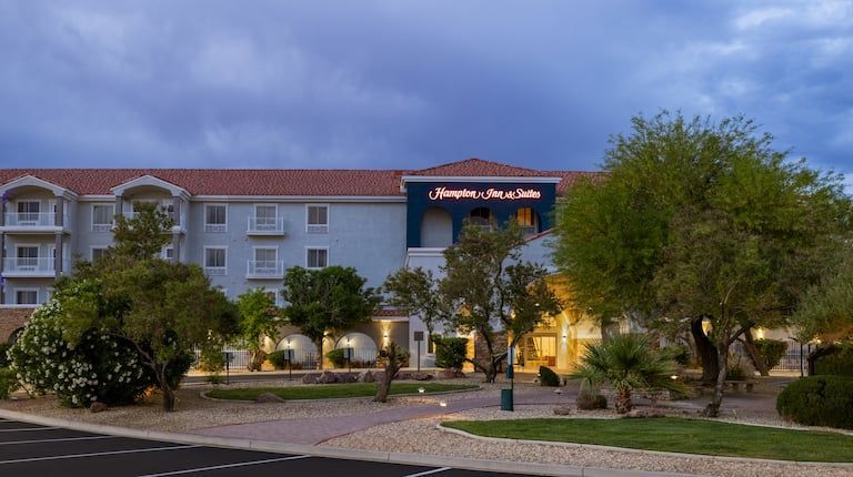 A large white building with a red tile roof is surrounded by trees and a parking lot.