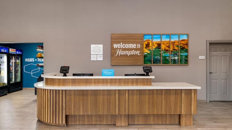 A hotel lobby with a wooden reception desk and a welcome sign on the wall.