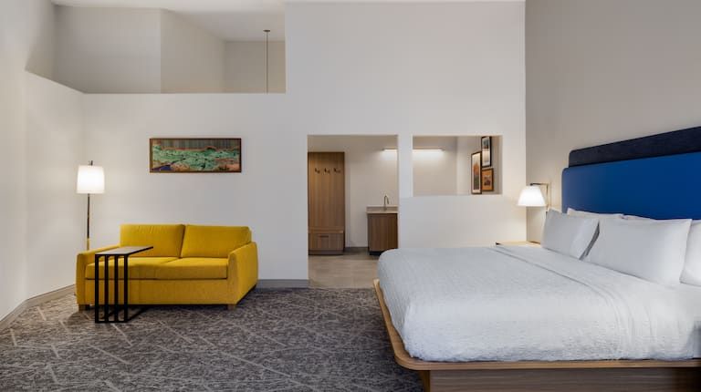 A hotel room with a king size bed and a yellow couch.