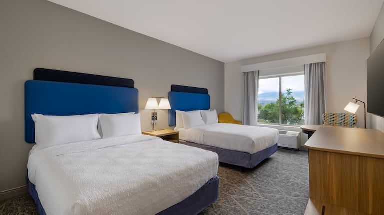 A hotel room with two beds , a dresser , a television and a window.