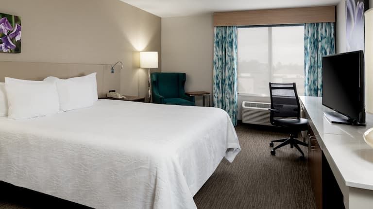A hotel room with a king size bed , desk , chair and television.