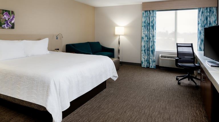 A hotel room with a king size bed , desk , chair and television.