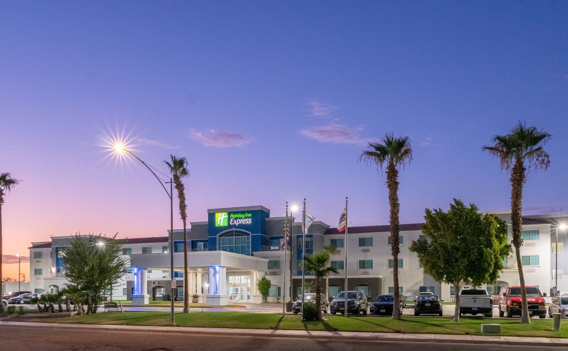 A large hotel with palm trees in front of it at night.