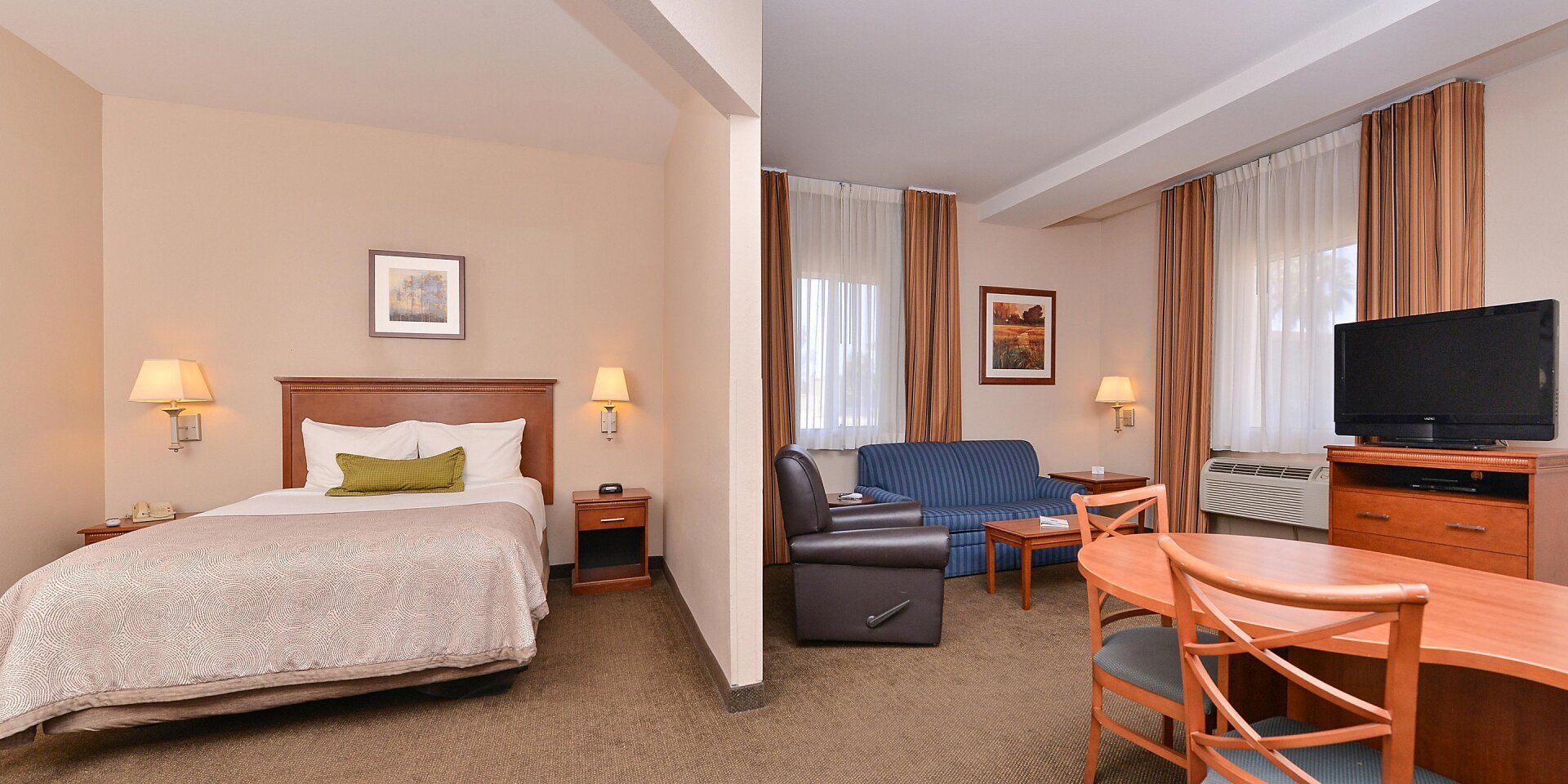 hotel bed and living room area with two couches, table, chairs, and television