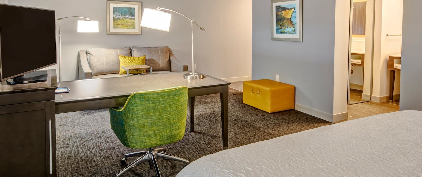 view of the hotel living room area with a desk, green chair and television