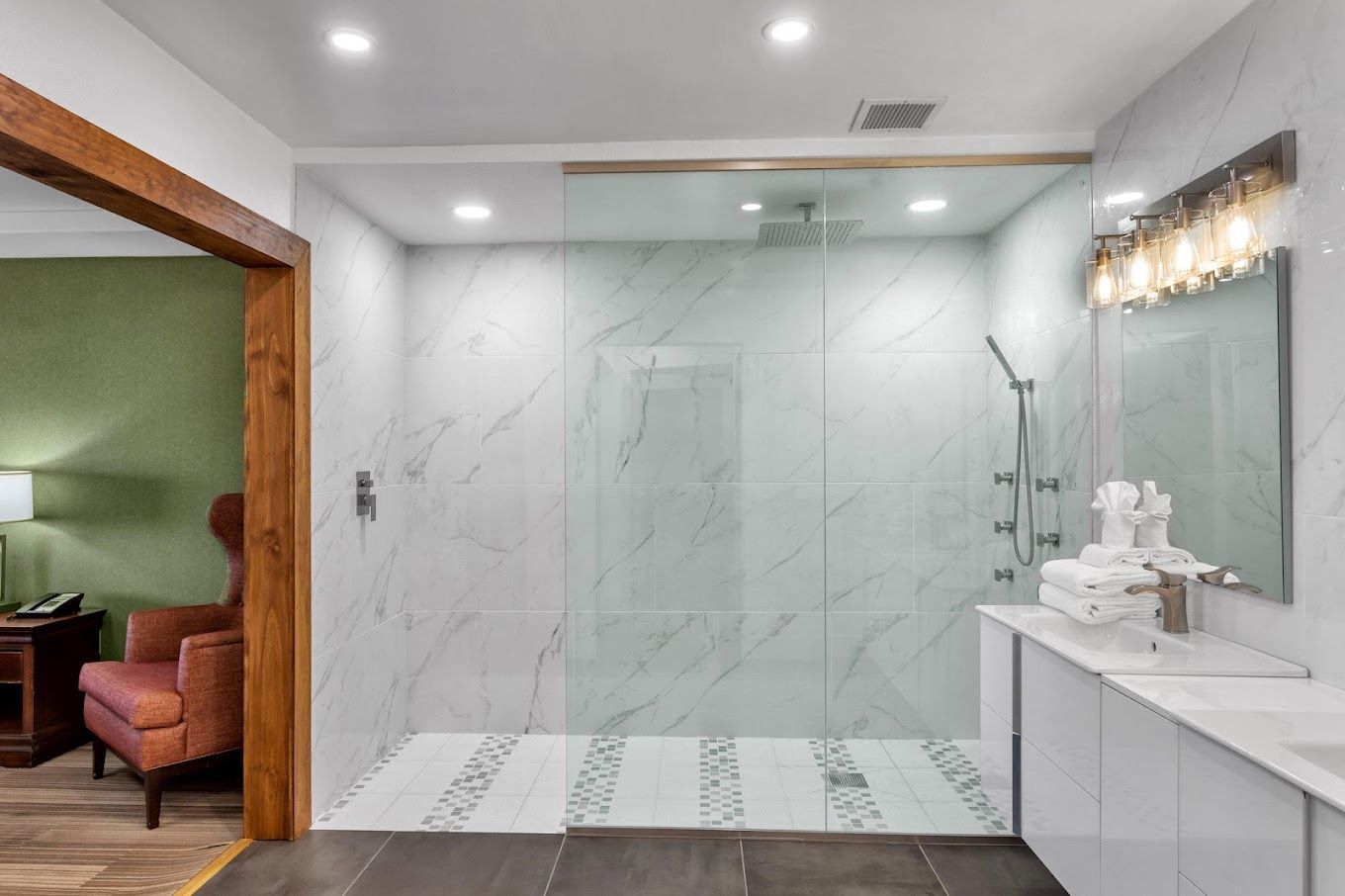 A bathroom with a walk in shower , sink , mirror and chair.