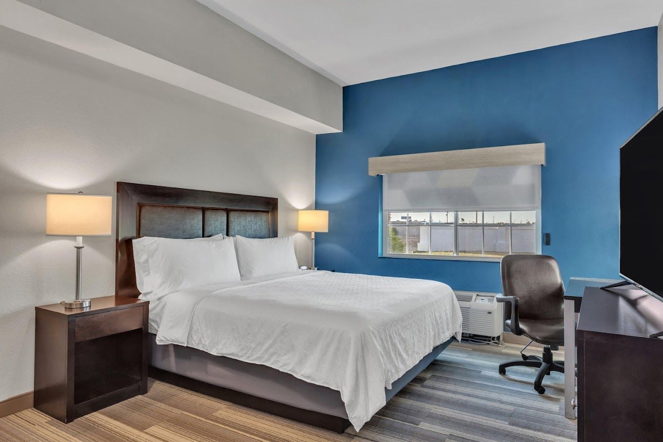 A hotel room with a king size bed , desk , chair and television.