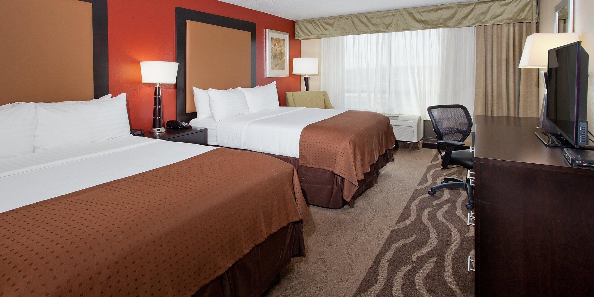 two comfortable hotel beds with brown decorative sheets and a lamp on the bedside