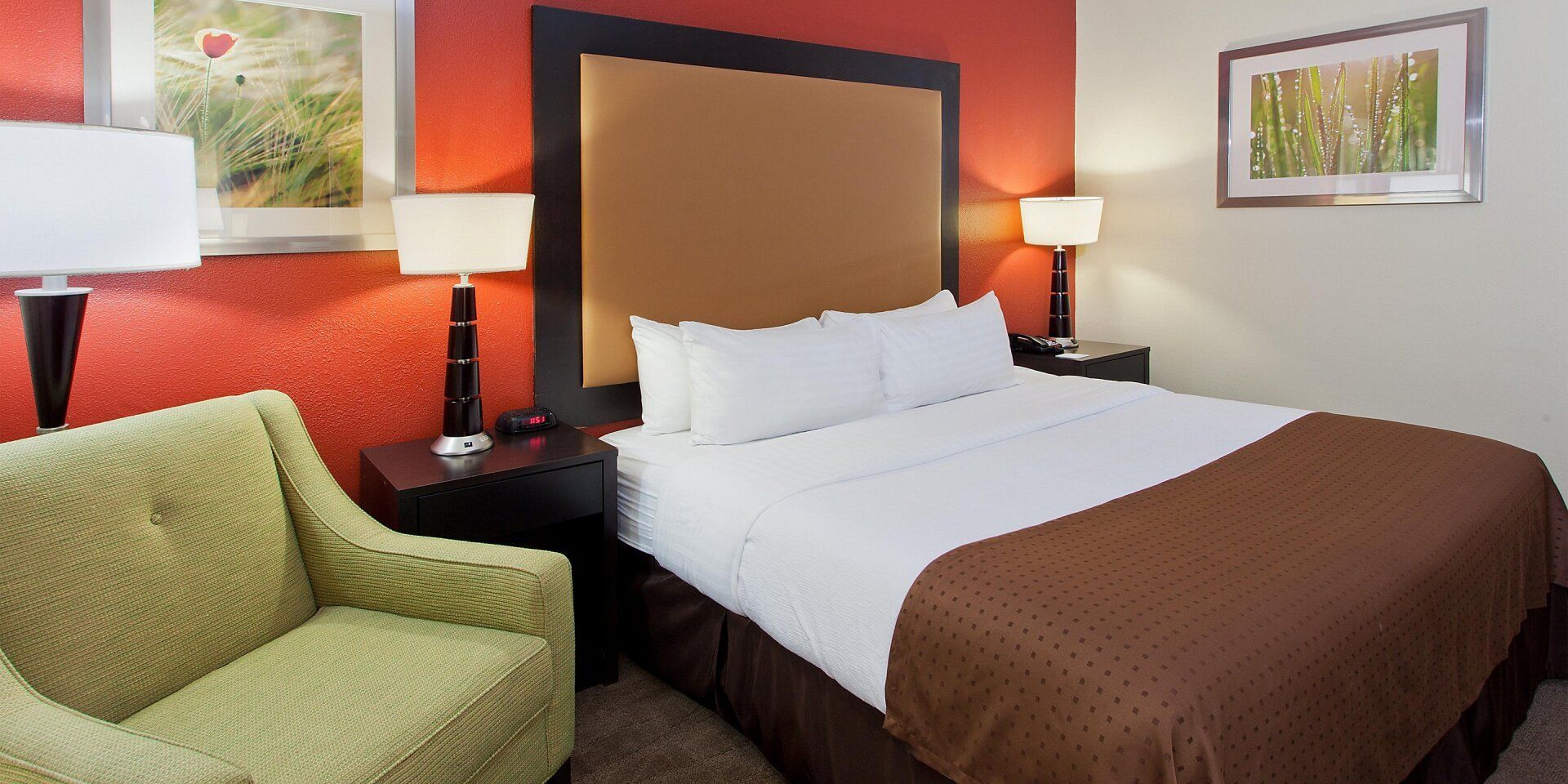 view to the hotel bed with lamps on both sides of the bed and a green seat