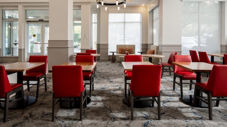 A dining room with red chairs and tables in a hotel.