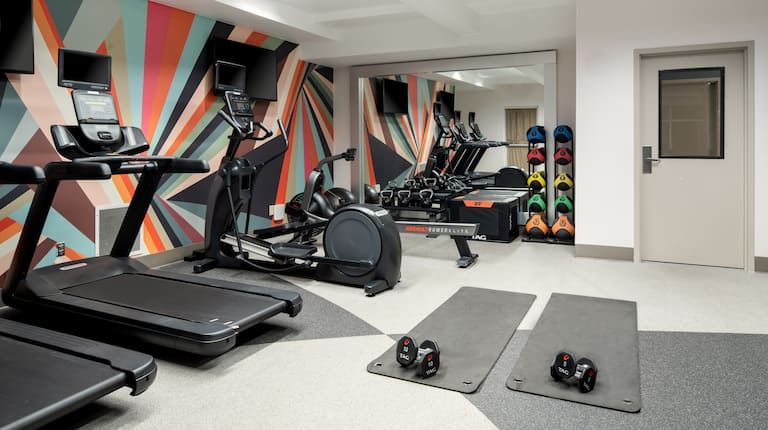 A gym with treadmills , ellipticals , and a large mirror.