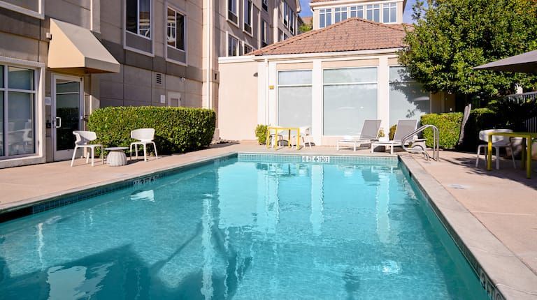 A large swimming pool surrounded by chairs and tables in front of a building.