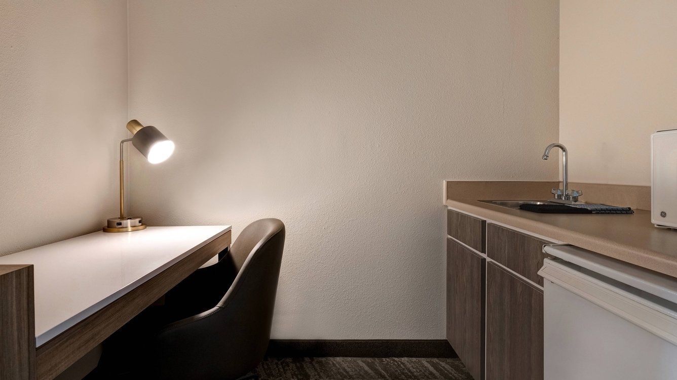 close up of the hotel room desk, lamp and chair with a sink in the back