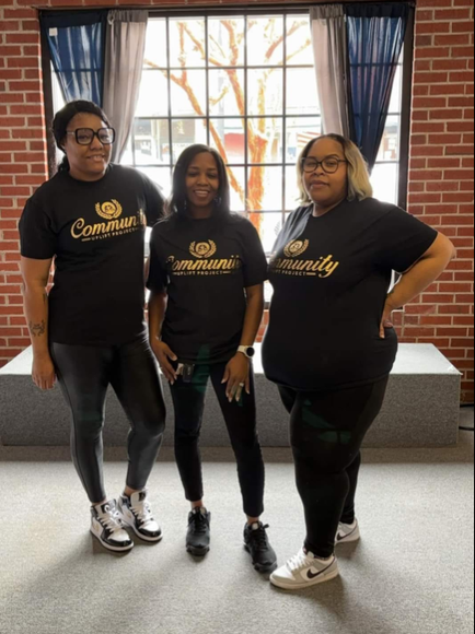Three women wearing black shirts with the word community on them