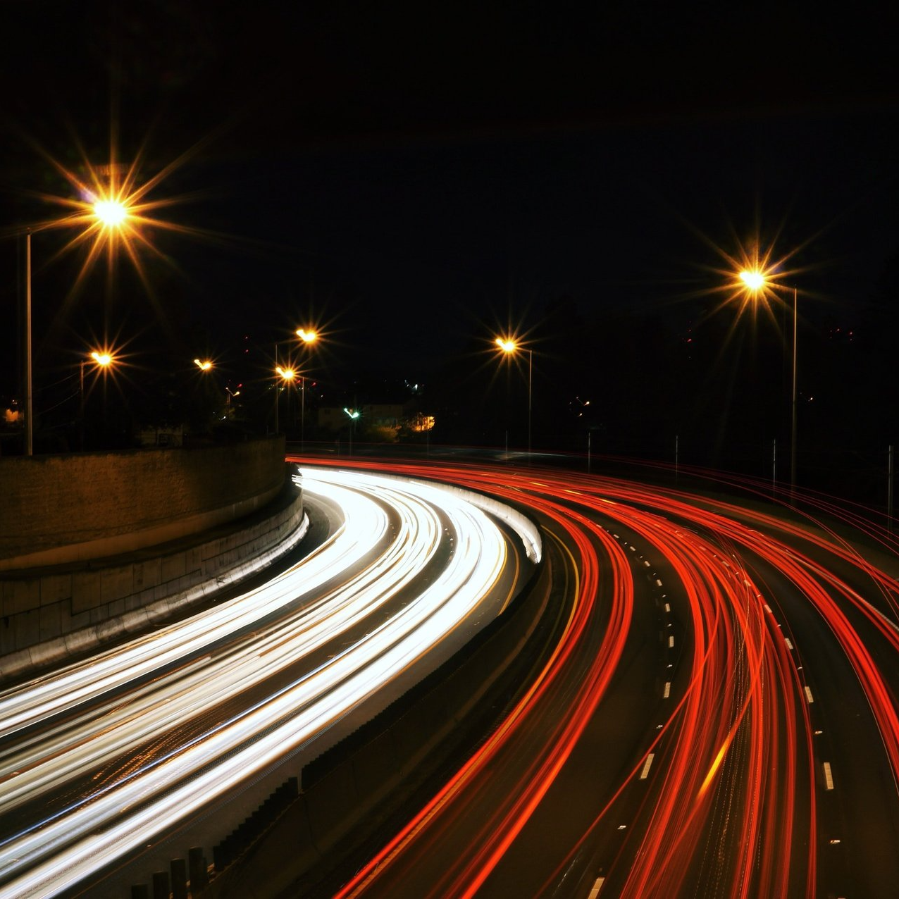 Photograph of a time lapse of a busy motorway at night. White and Red lights