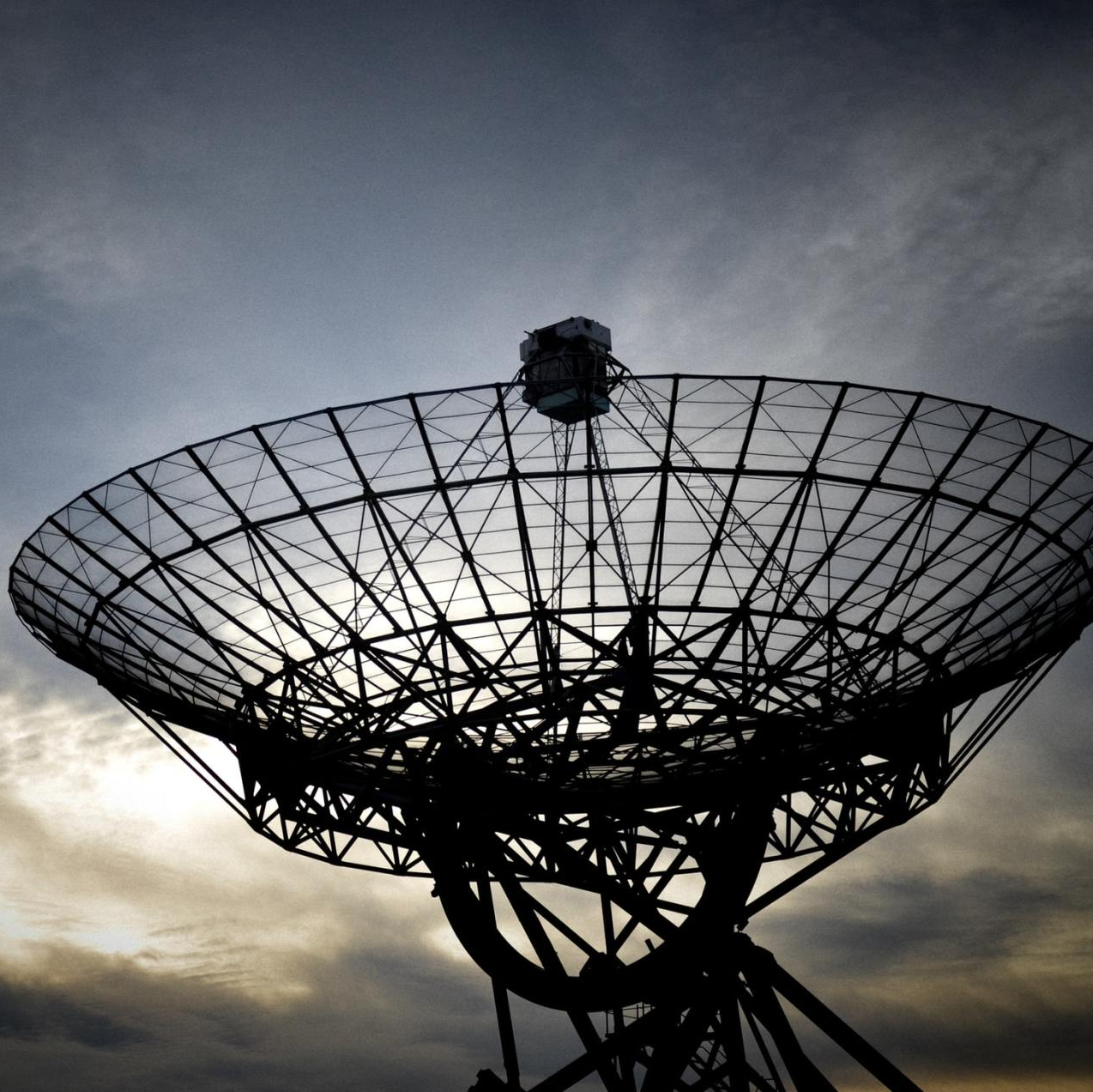 Photograph of a radio telescope against the blue sky with clouds