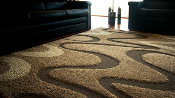 Brown and tan patterned rug with two black leather sofas in a living room.