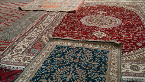 Assorted ornate oriental rugs, red, teal, and cream, displayed on a floor.