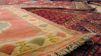 Close-up of several colorful oriental rugs, some partially rolled, with detailed patterns and fringe.