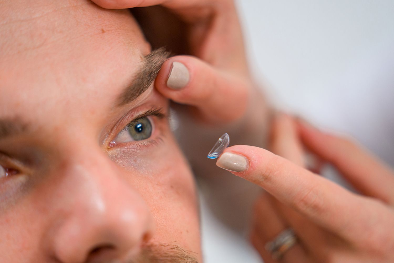 A close up of a person putting a contact lens in a man 's eye.