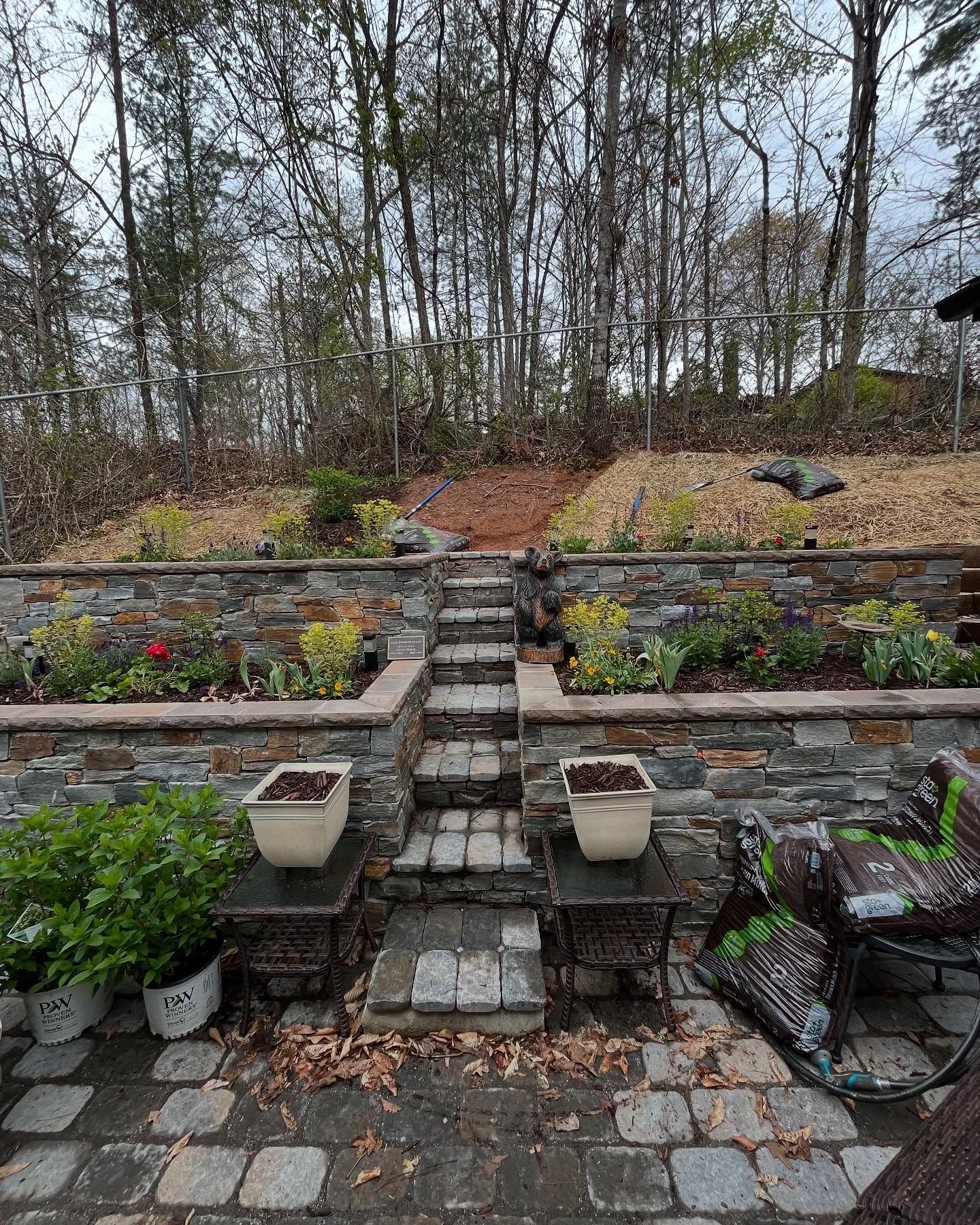 Stone terraced garden with steps and potted plants, leading to a wooded hillside.