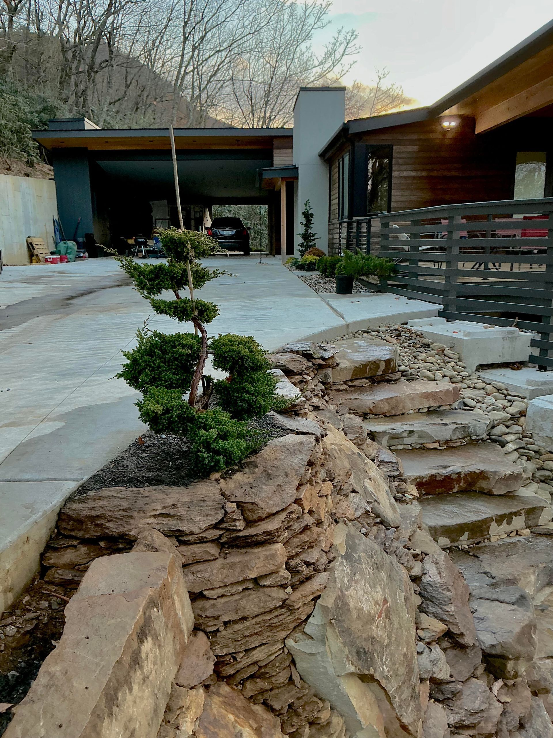 Exterior of modern house with rock steps, driveway, and manicured shrub.