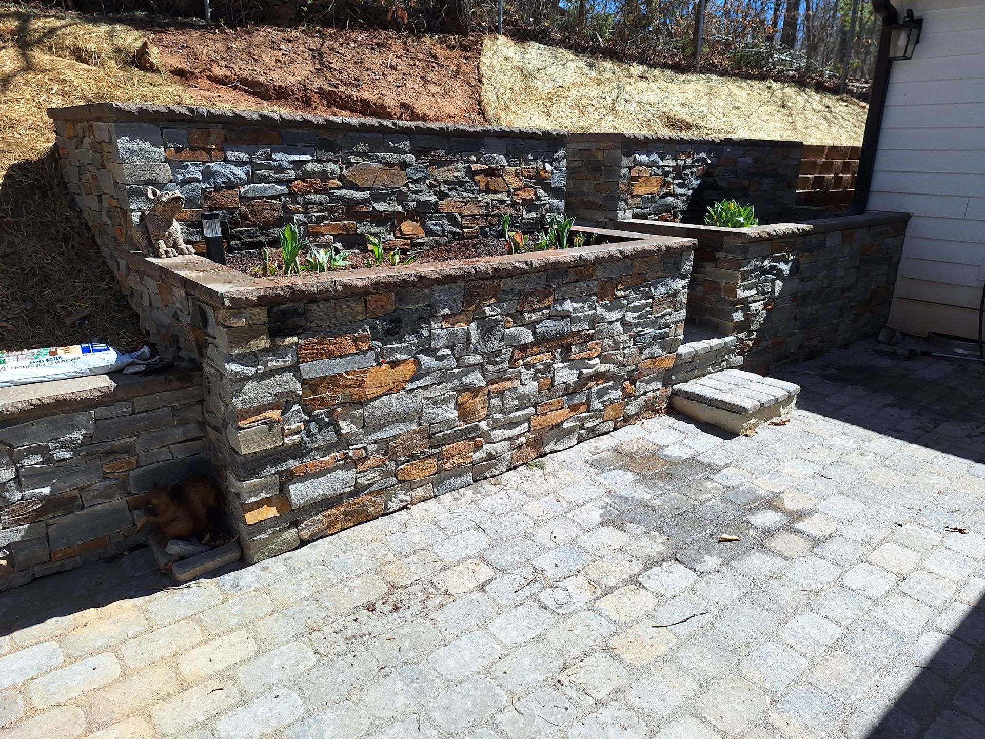 A stone wall is surrounding a brick patio.