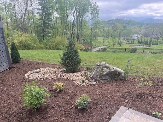 Landscaped yard with a rock feature, trees, and a view of mountains.