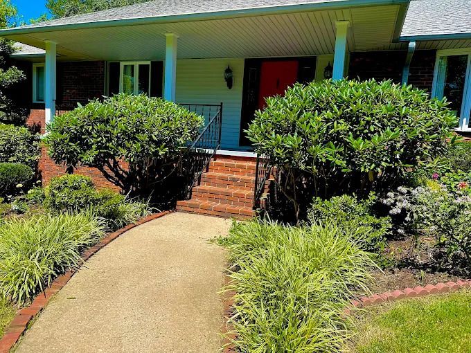 Exterior view of a house with a red door, brick walkway, and green bushes.