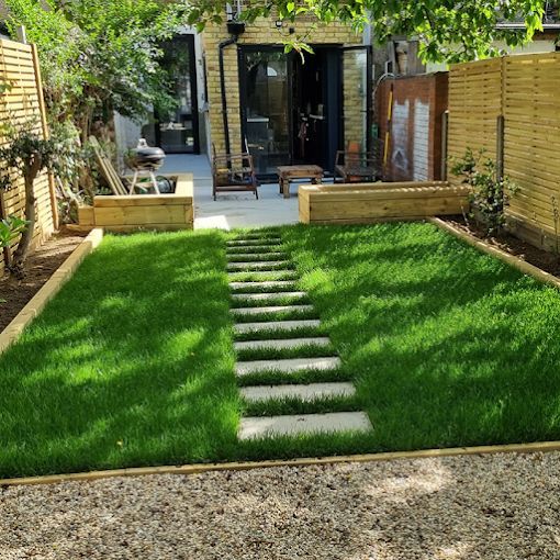 Green backyard with a stone path leading to a house with an open back door and furniture.