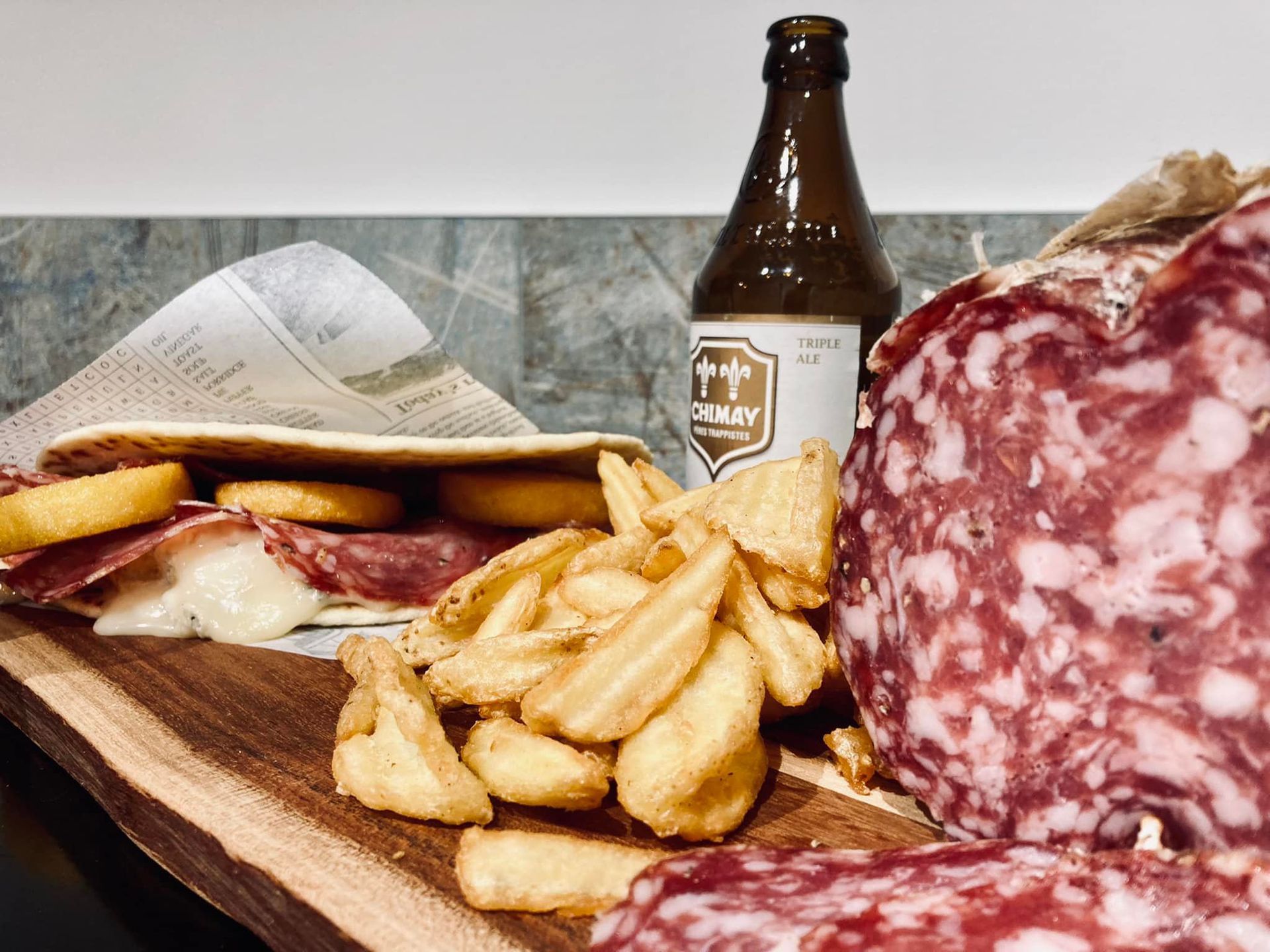 Una bottiglia di birra è appoggiata accanto a un panino e a delle patatine fritte su un tavolo di legno.