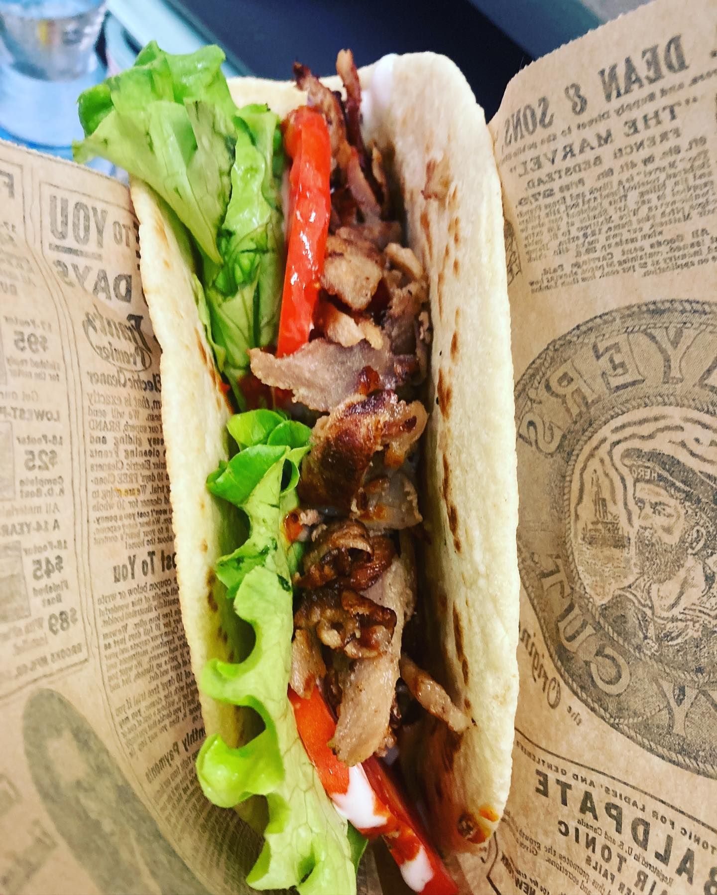 Un taco con lattuga, pomodori e carne è avvolto in un giornale