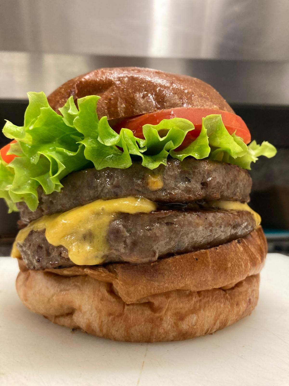 Un doppio cheeseburger con lattuga, pomodoro e formaggio, servito in un panino su un tagliere.
