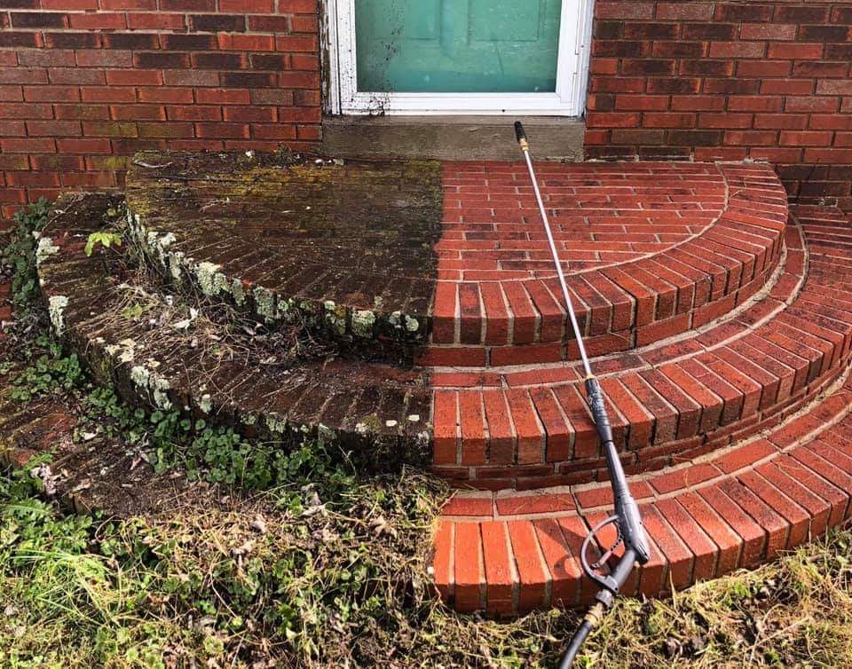 Brick steps being pressure washed, revealing a clean, red right side and dirty, moss-covered left side.