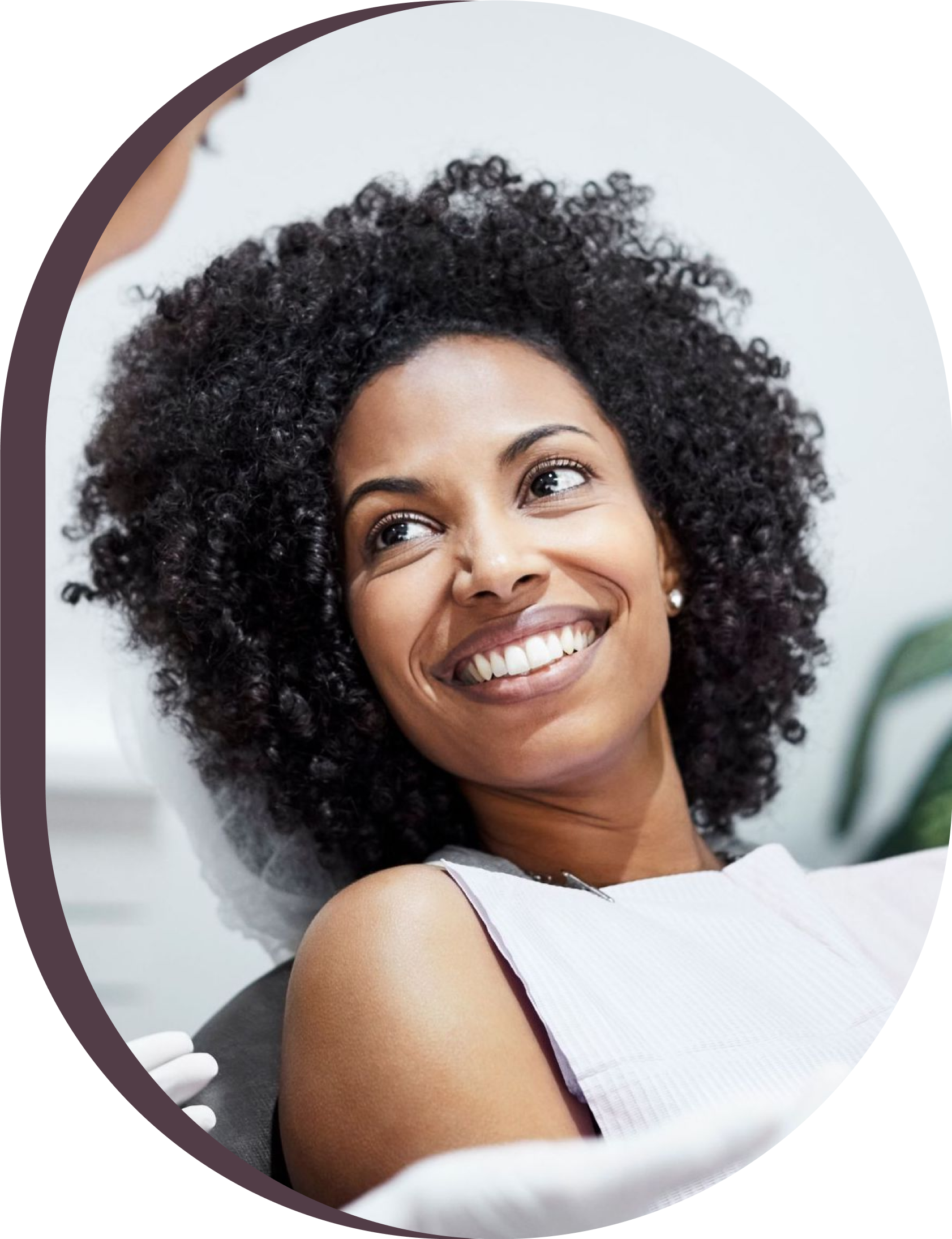 A woman with curly hair is smiling while sitting in a dental chair