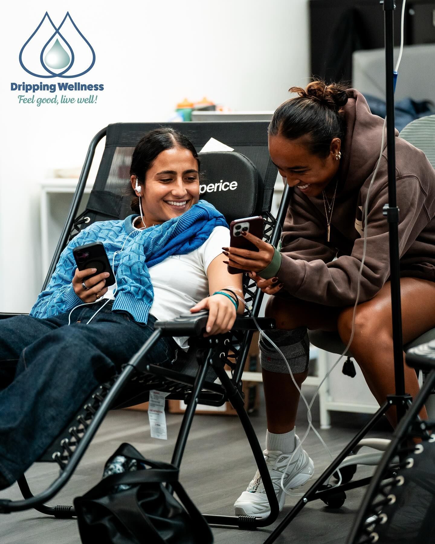 Two people smile while using IV drips and phones, in a relaxed setting.