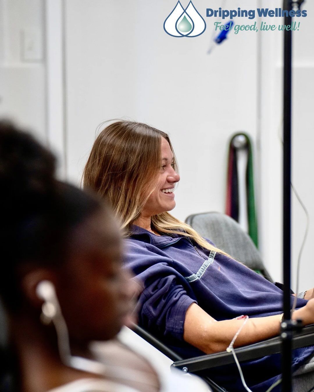 Woman smiles while receiving IV drip at Dripping Wellness clinic.