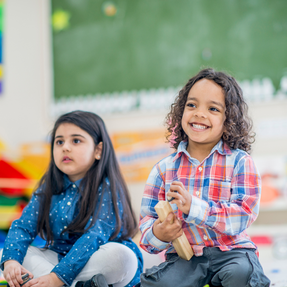 A boy and a girl are sitting on the floor in a classroom.