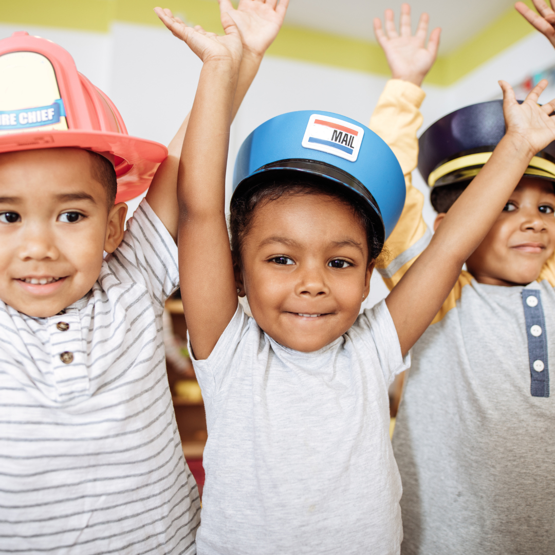 Three children wearing hats with one that says fire chief