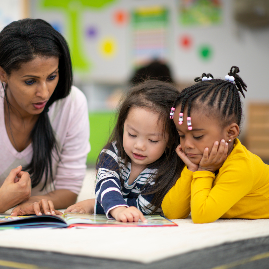 A woman is reading a book to two little girls.
