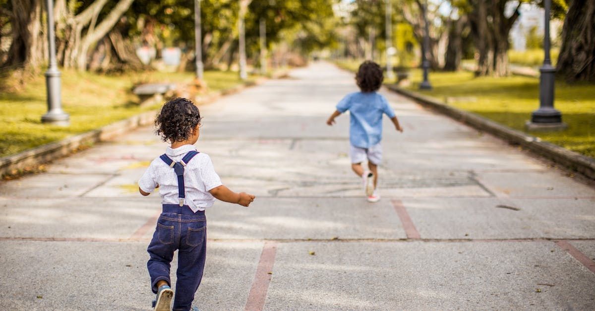 Two young boys are running down a road in a park.